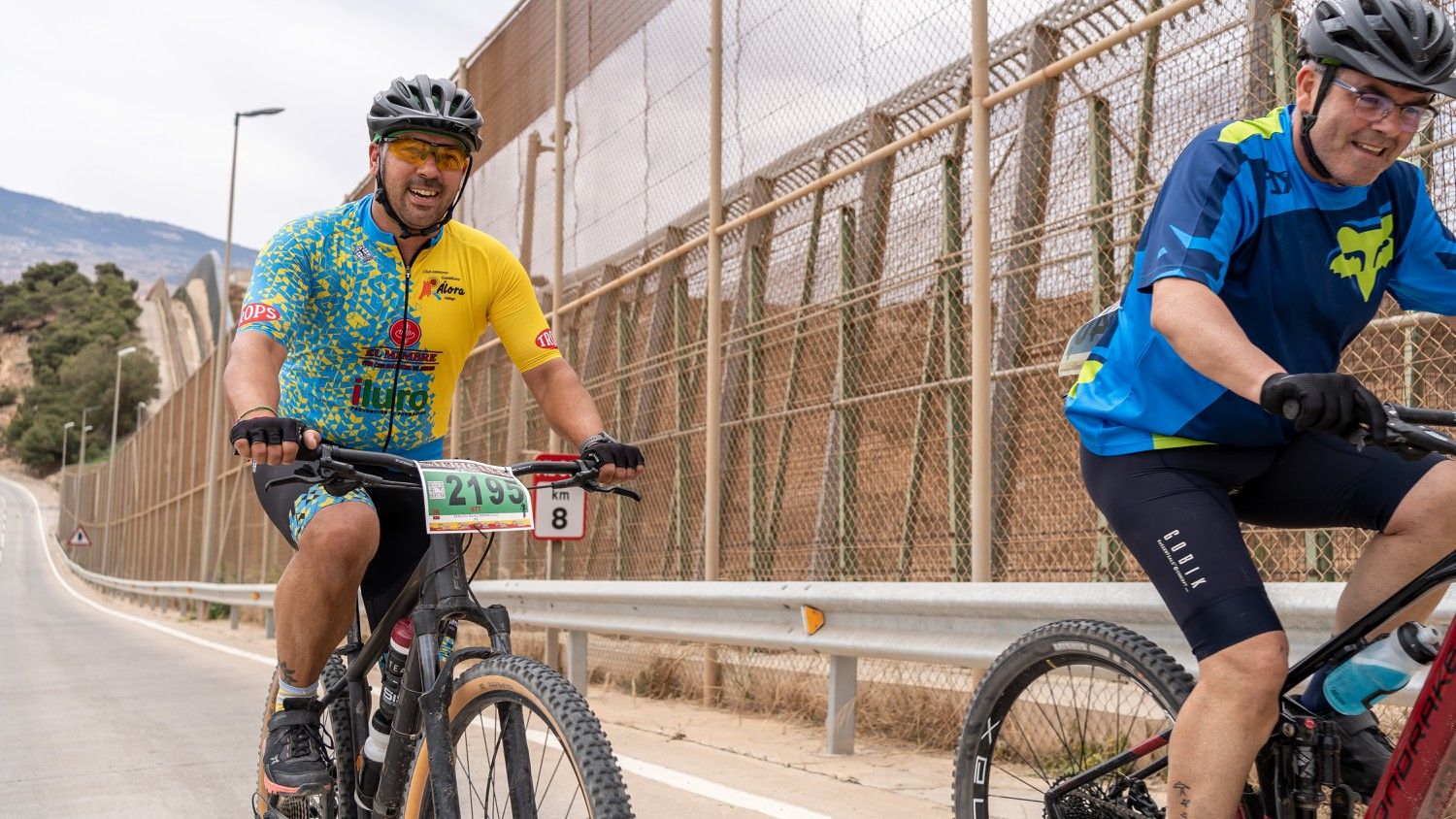 Dos ciclistas ruedan junto a la valla fronteriza