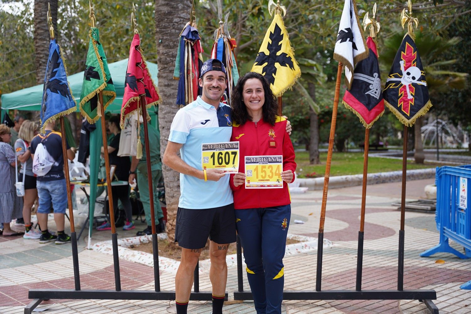 Dos participantes posan con sus dorsales entre banderas de La Legión