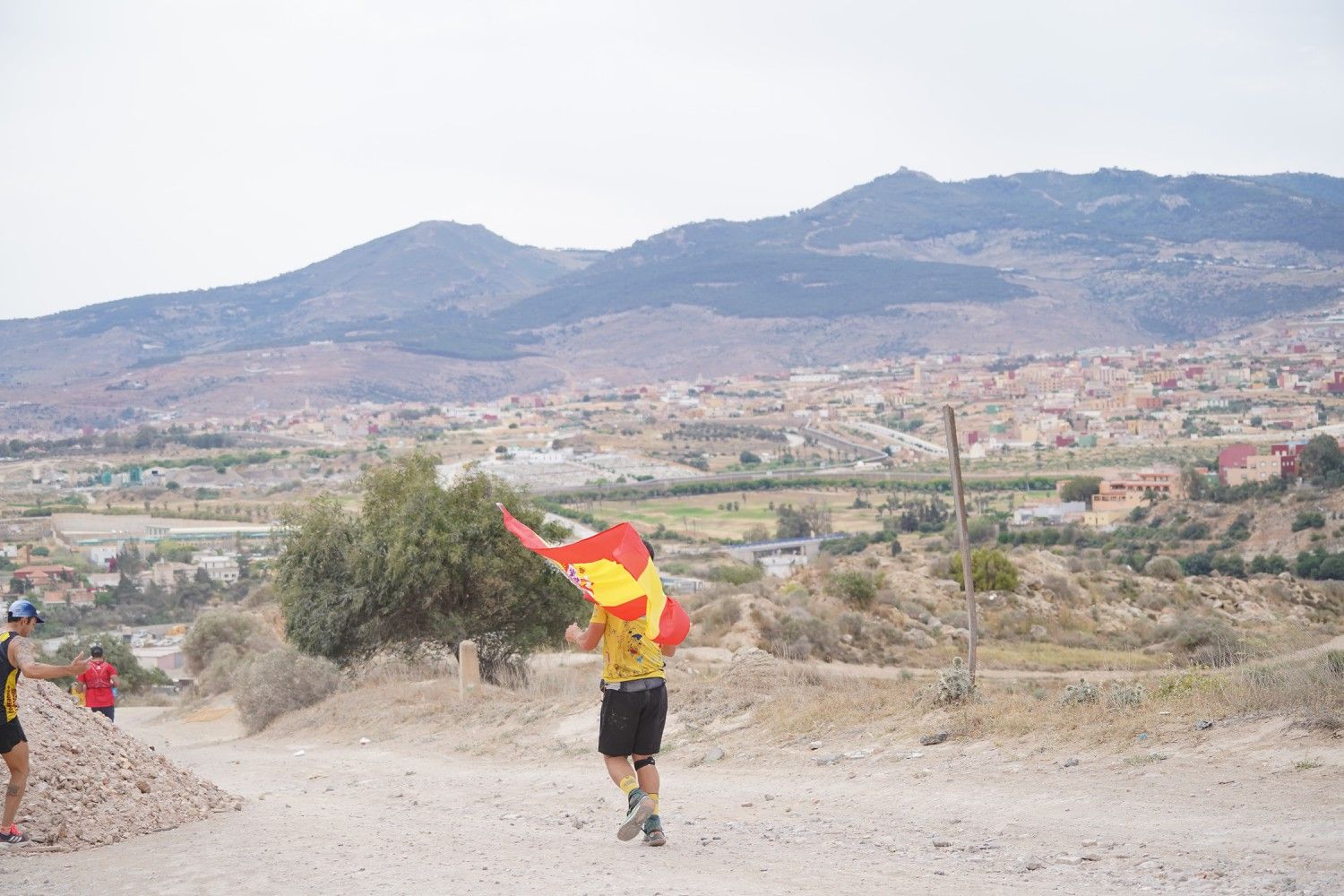 Un corredor con una bandera de España en un paraje con montes al fondo