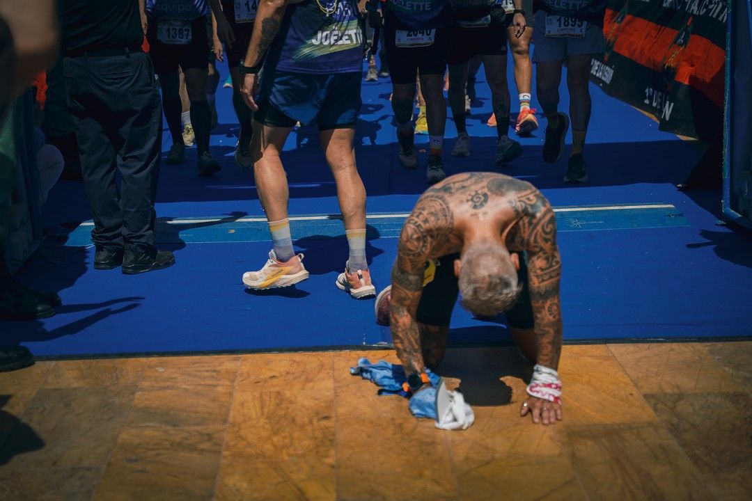 Un participante, exhausto, se arrodilla en la alfombra azul tras cruzar la meta